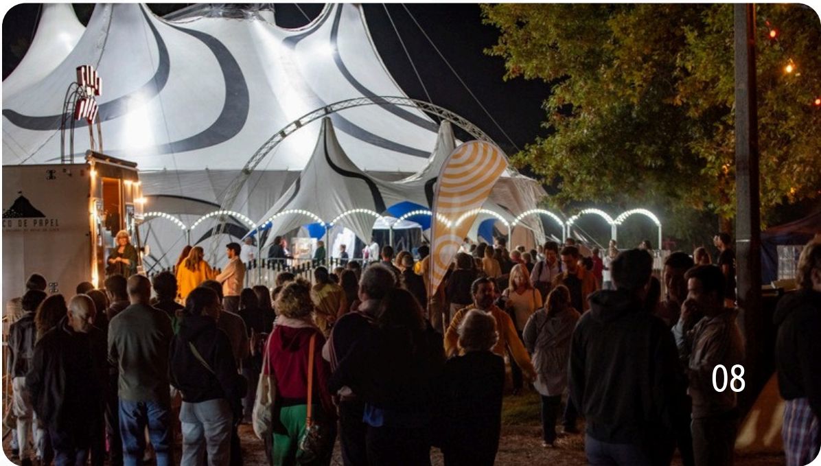 Público junto à tenda de circo branca iluminada à noite