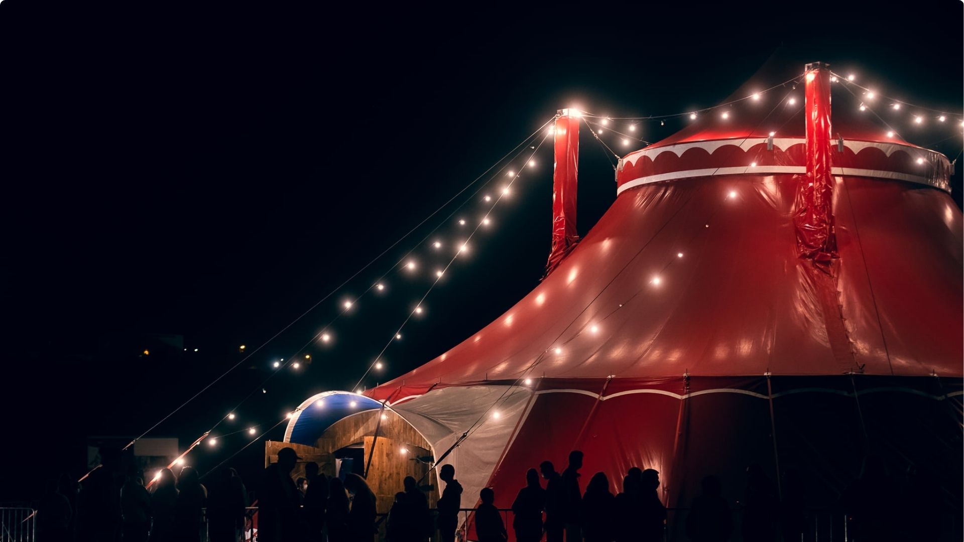 Tenda de circo iluminada à noite com público à entrada